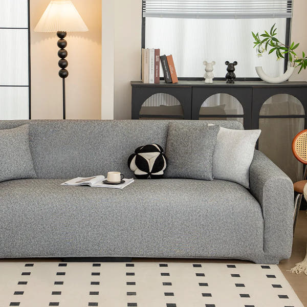 Sofa dressed in stone grey knit cover in a living room, angled view with a ball cushion and coffee cup.