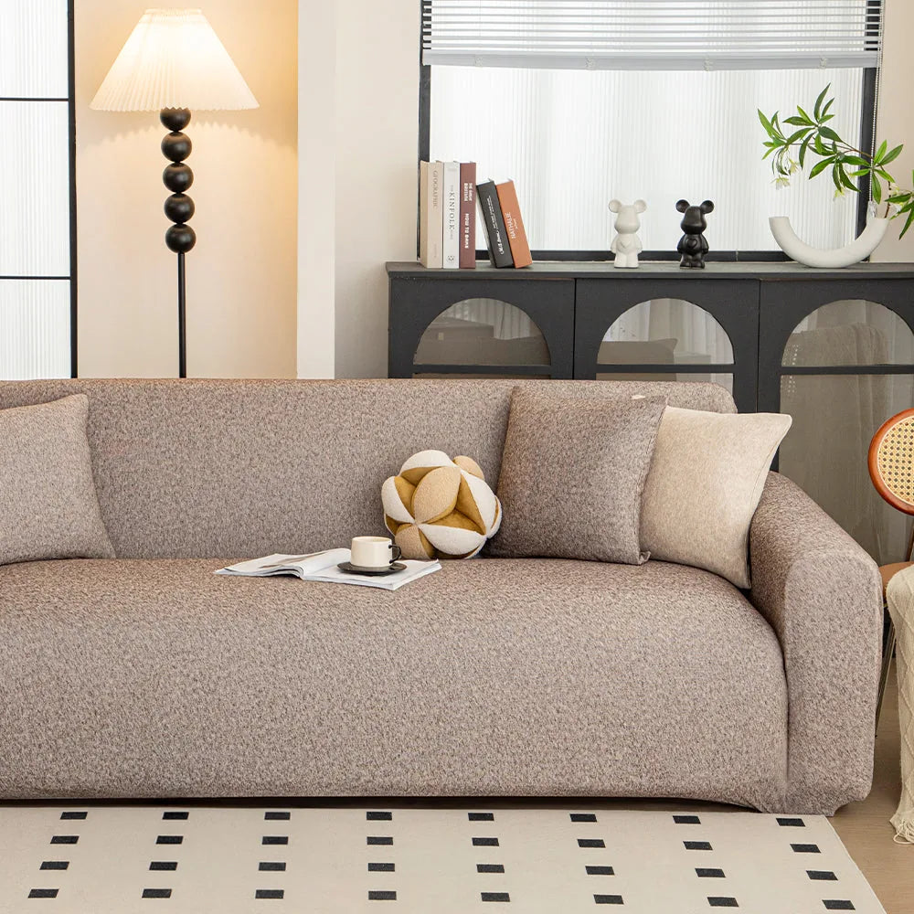 Sofa dressed in warm taupe knit cover in a bright living room, angled view with a ball cushion and cup.