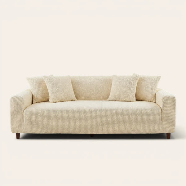 Cream ivory quilted sofa cover fitted on a three-seat couch with matching cushions, front view on ivory.
