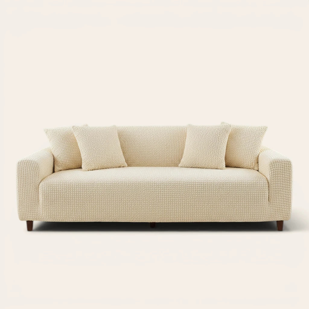 Cream ivory quilted sofa cover fitted on a three-seat couch with matching cushions, front view on ivory.