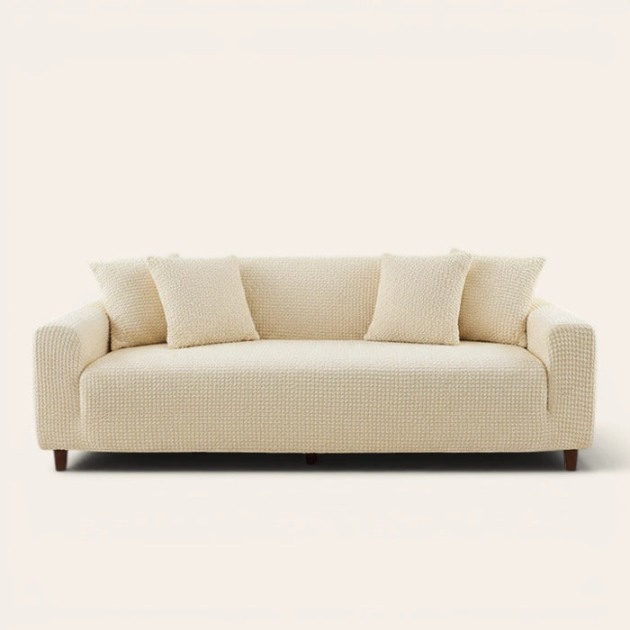 Cream ivory quilted sofa cover fitted on a three-seat couch with matching cushions, front view on ivory.