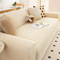 Sofa dressed in cream ivory quilted cover in a living room, angled view with bolster and polka dot cushions.