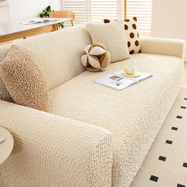 Sofa dressed in cream ivory quilted cover in a living room, angled view with bolster and polka dot cushions.