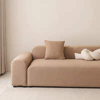 Sofa dressed in caramel sand smooth cover in a bright living room, angled side view with cushion.