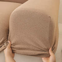 Hands stretching the caramel sand cover snugly around a rounded sofa armrest corner.