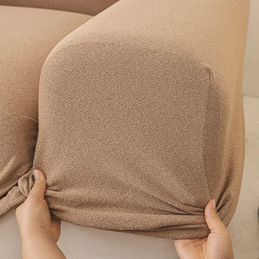 Hands stretching the caramel sand cover snugly around a rounded sofa armrest corner.