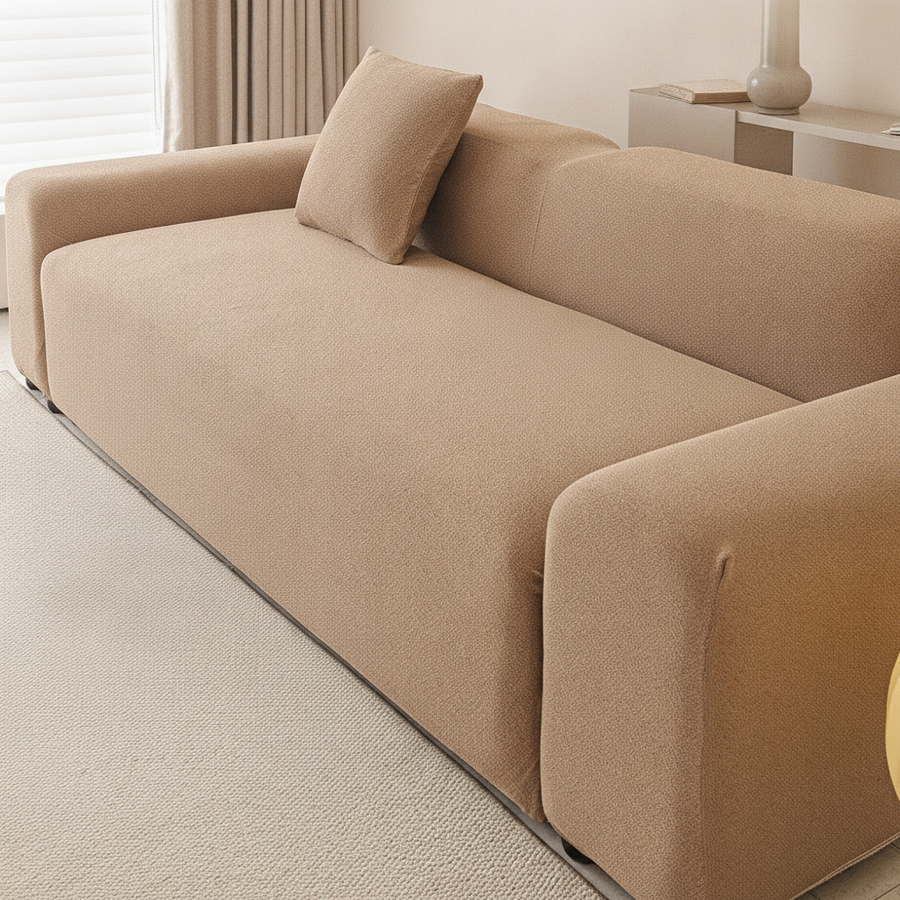 Three-seat sofa in caramel sand smooth cover with a bolster pillow, angled living room view.