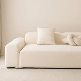 Cream smooth stretch sofa cover styled on a corner sofa with a cushion and knot pillow