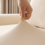 Hand stretching the cream sofa cover to show its flexible fit