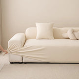 Hands pulling the cream stretch sofa cover snug over a three-seat sofa