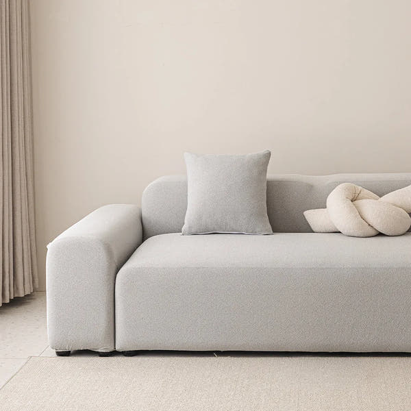 Silver grey smooth stretch sofa cover styled on a corner sofa with a cushion and knot pillow