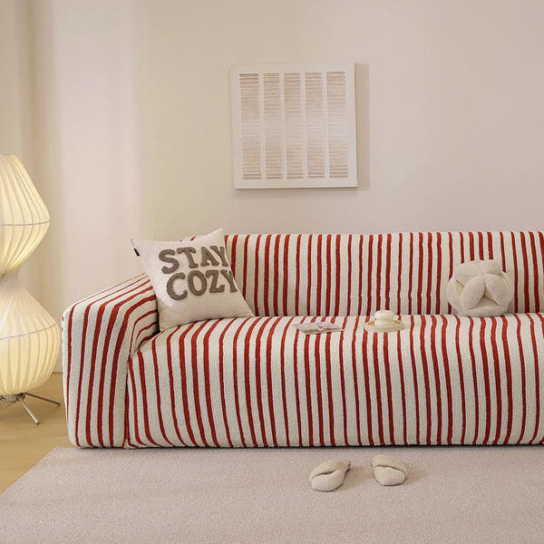 Crimson red striped stretch sofa cover styled in a warm living room with a cushion