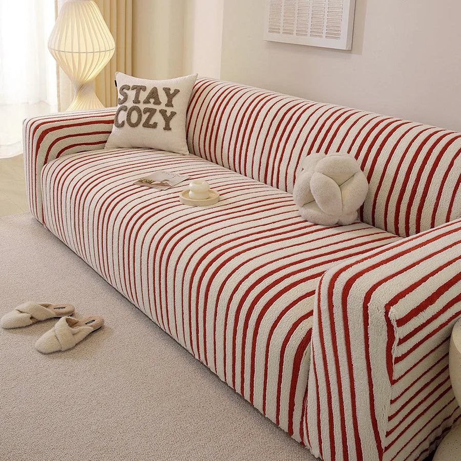 Corner detail of the crimson red striped sofa cover wrapping the armrest near a soft lamp