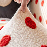 Hand lifting the stretchy cream red teddy sofa cover to show its raised red dots