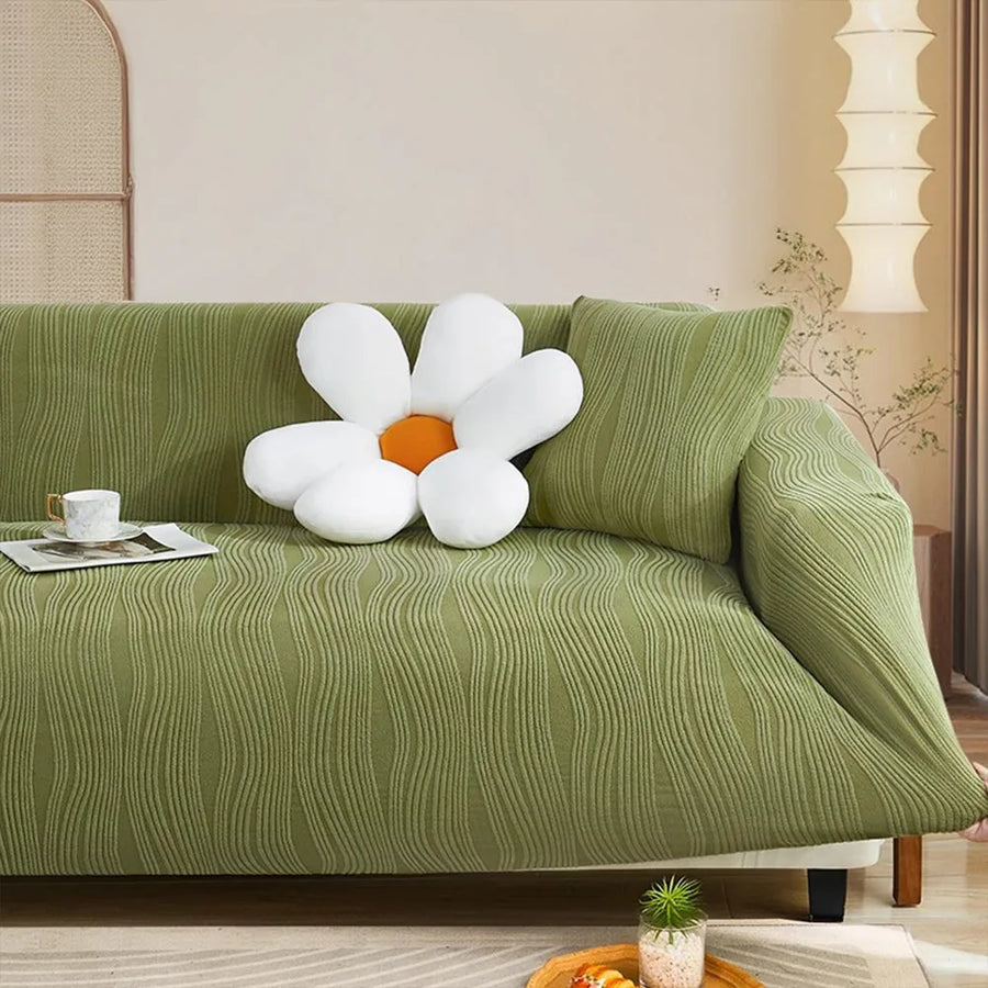 Corner view of the sage green velvet sofa cover with an accent cushion beside a floor lamp