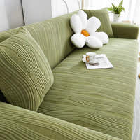 Angled view of the sage green velvet sofa cover across an L-shaped seat with cushions