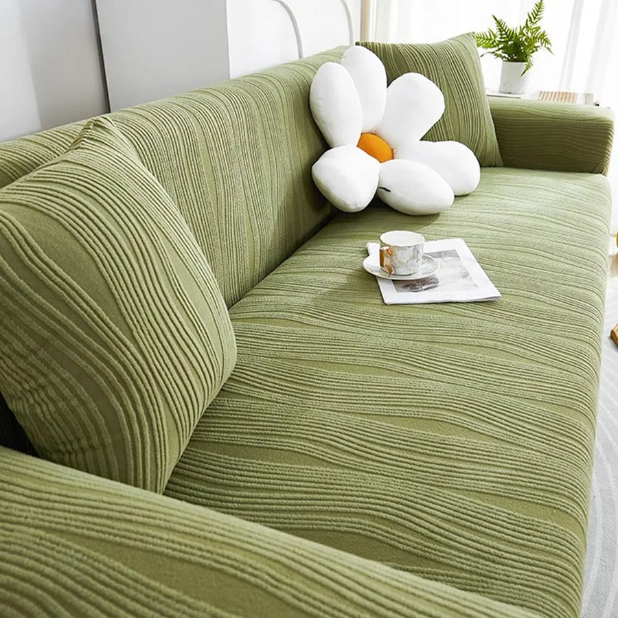 Angled view of the sage green velvet sofa cover across an L-shaped seat with cushions