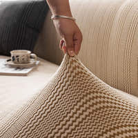 Hand lifting the elastic almond cream waffle sofa cover to show its stretch fit