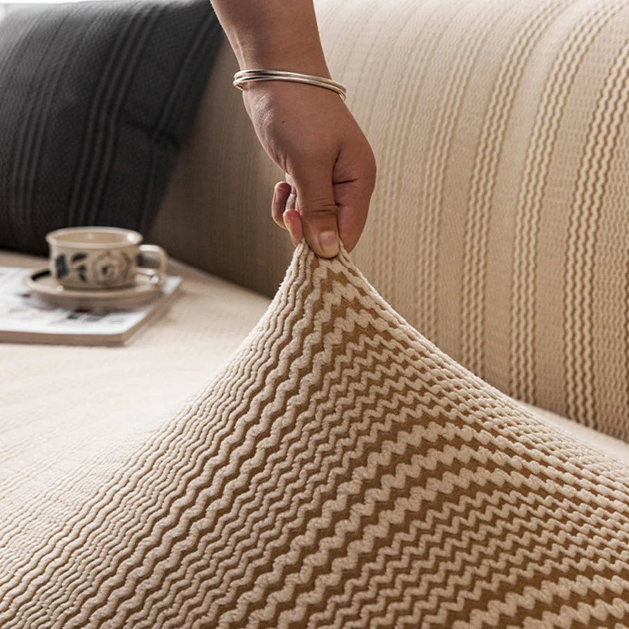 Hand lifting the elastic almond cream waffle sofa cover to show its stretch fit