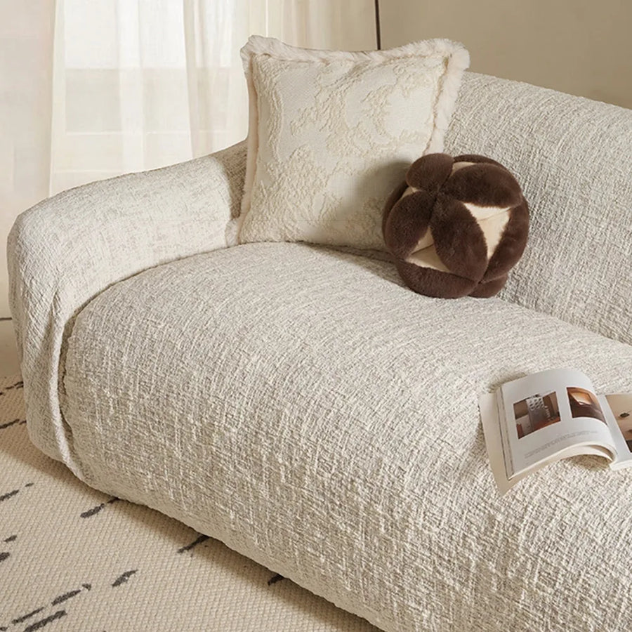 Ivory cream woven sofa cover draped over a chaise section beside sheer curtains and cushions