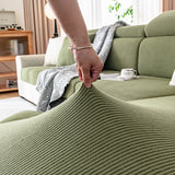 A hand lifting the corner of an olive green corduroy cover to show how far the fabric stretches