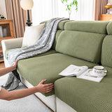 Fitting an olive green corduroy cover over a seat cushion, hands tucking the edge underneath