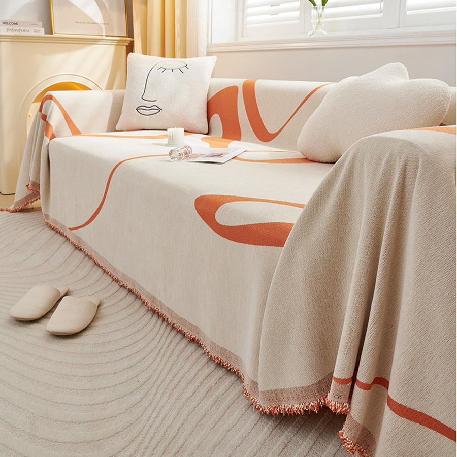 Angled view of the Sunset Stream Abstract Muse throw with fringed edge and slippers nearby