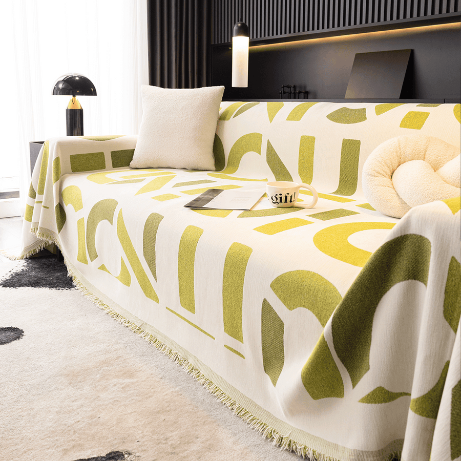 Whispering Fern Abstract Narratives throw on a corner sofa with cushion, book and coffee