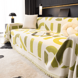 Whispering Fern Abstract Narratives throw on a corner sofa with cushion, book and coffee