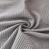 Macro close-up of the graphite mist throw's embossed geometric quilting swirled to show softness