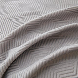 Close-up of the graphite mist throw's draped folds and raised geometric pattern in soft gray