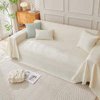 Artisan Cooling throw in Ivory Cloud over a sofa with cushions, lamp and side table, angle view
