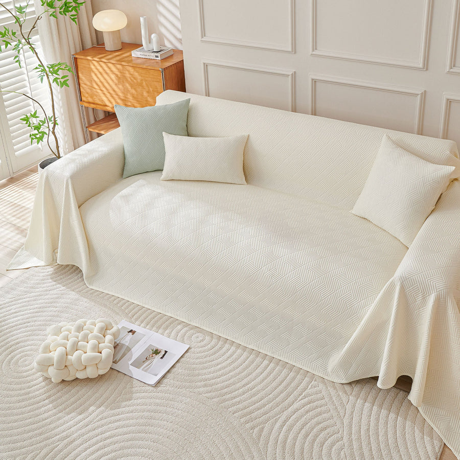 Artisan Cooling throw in Ivory Cloud over a sofa with cushions, lamp and side table, angle view