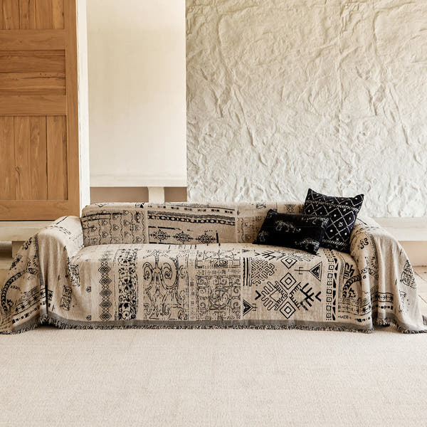 Sand beige glyph-print throw covering a sofa against a rustic stone wall with black cushion