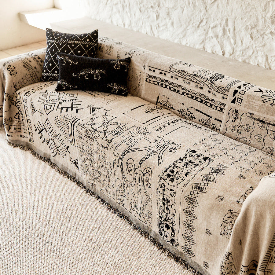 Sand beige glyph throw draped over a sofa beside a textured stone wall