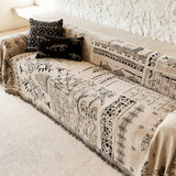Sand beige glyph throw draped over a sofa beside a textured stone wall