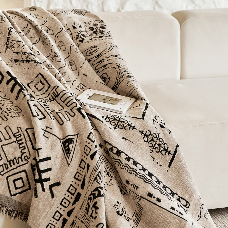 Sand beige glyph throw draped across a cream sofa with an open book
