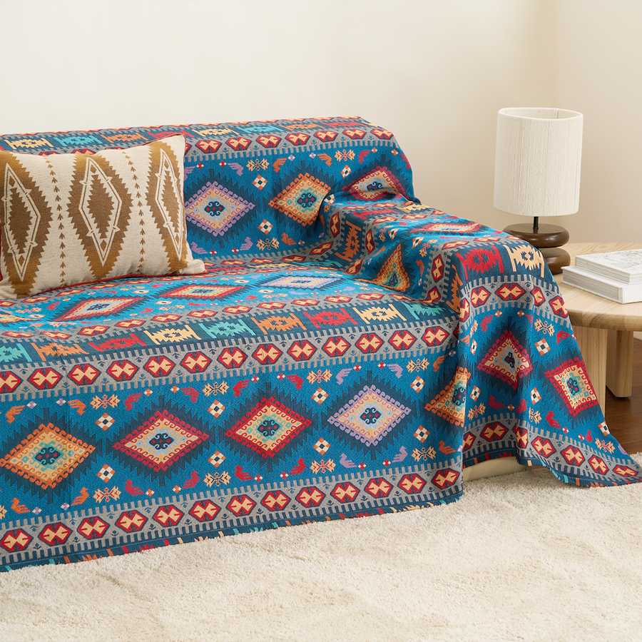 Indigo Oasis Azure Boho throw draped over a sofa arm and seat, three-quarter view with side table