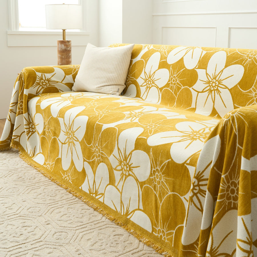 Angled view of the Bloom Elegance golden bloom throw over a sofa with a ribbed cushion and fringed hem