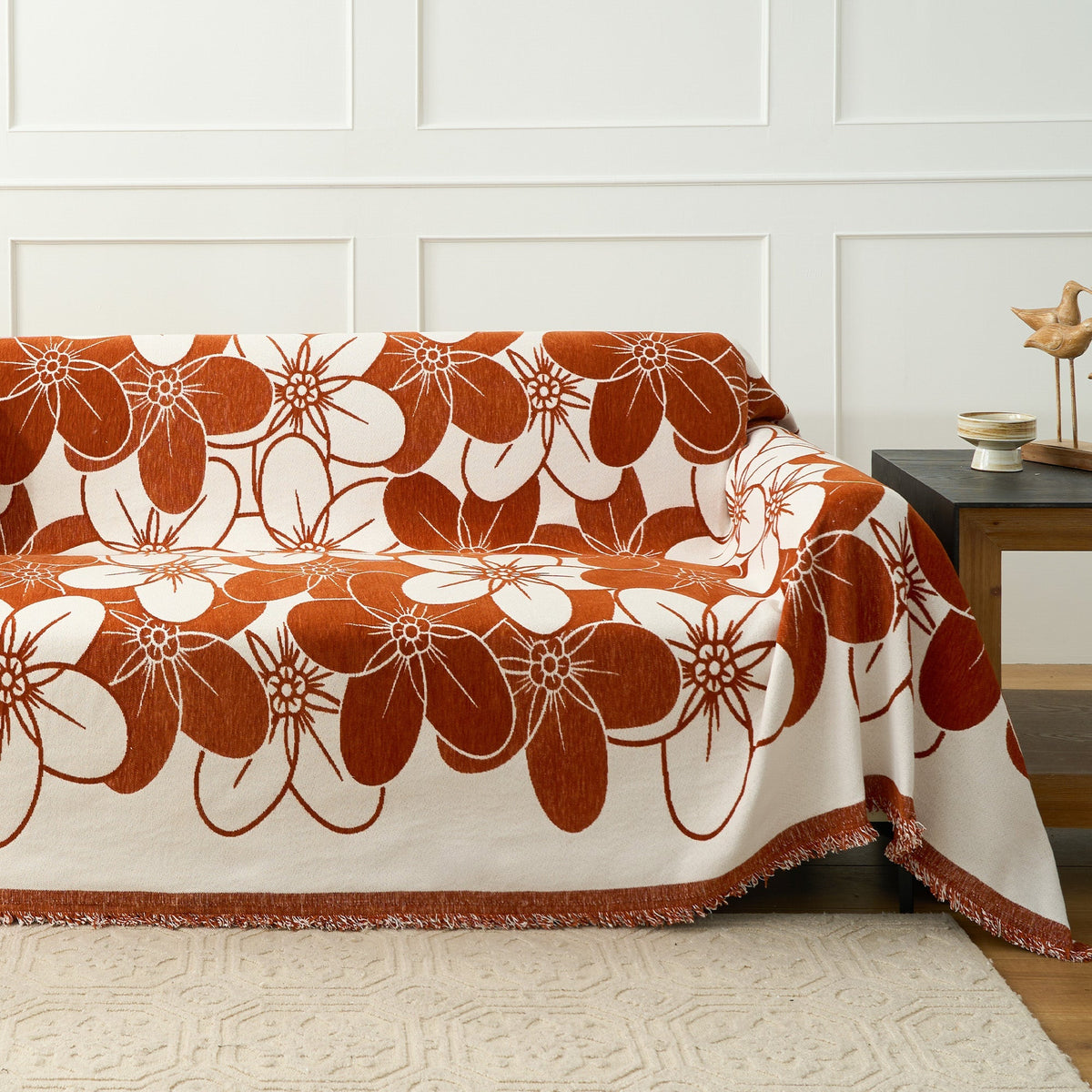 Rust floral blossom throw covering a sofa near a wood side table and panelled wall