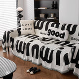 Angled corner view of the Bold Typography graphic harmony throw with a LOVE HOME cushion and coffee cup