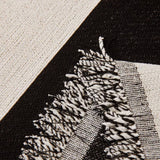 Detail of the graphic harmony Bold Typography throw's tasseled fringe in black and cream