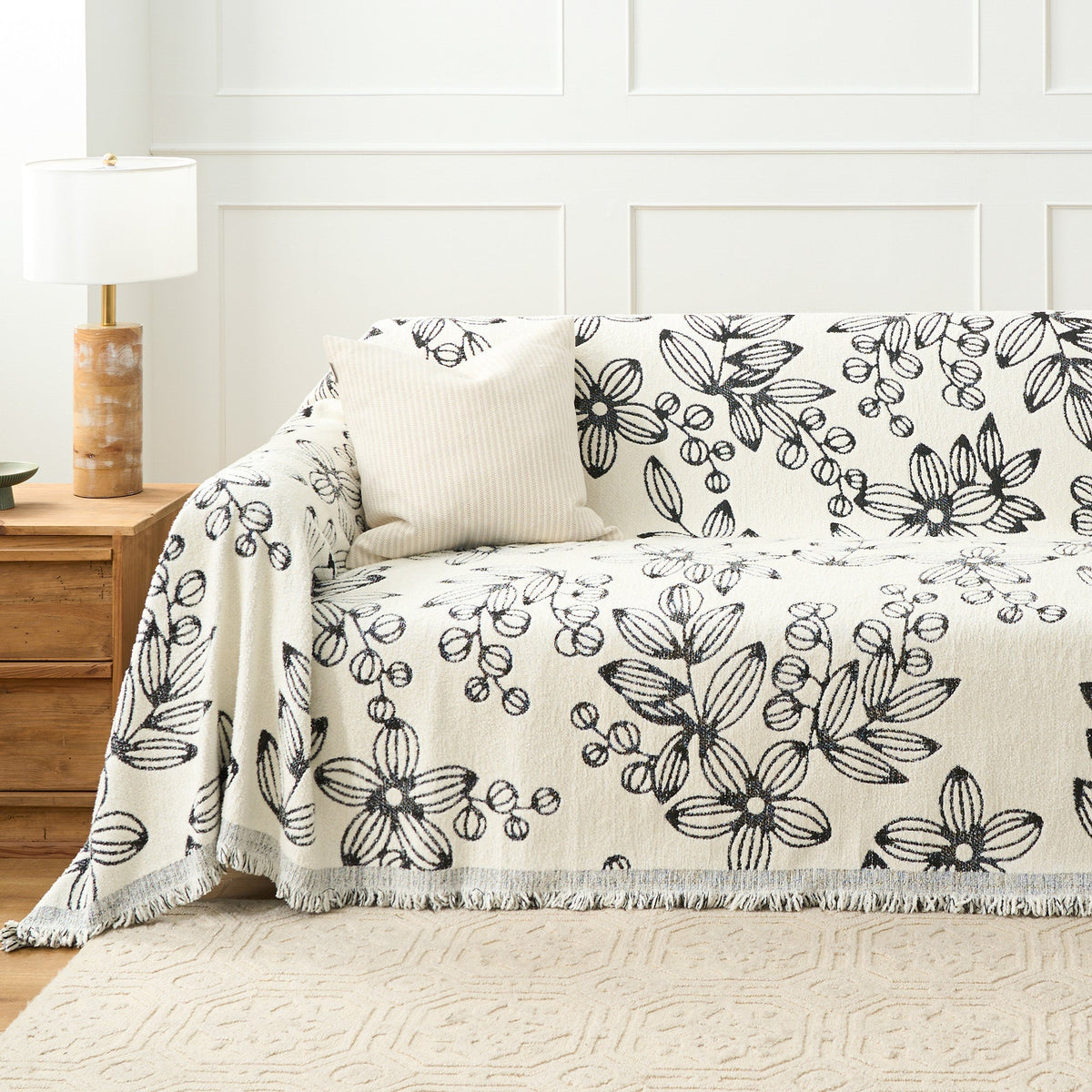 Botanic Sketch floral throw styled on a sofa against a paneled wall with a ribbed cushion and lamp