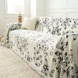 Angled view of the Botanic Sketch throw on a sofa by a window, showing its reversible side
