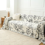 Wider view of the Botanic Sketch floral throw covering a sofa beside a wood lamp