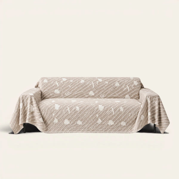 Linen Beige Botanical Quilted sofa throw draped over a two-seat sofa, front view on ivory background, white leaf motifs