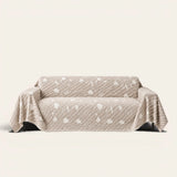 Linen Beige Botanical Quilted sofa throw draped over a two-seat sofa, front view on ivory background, white leaf motifs