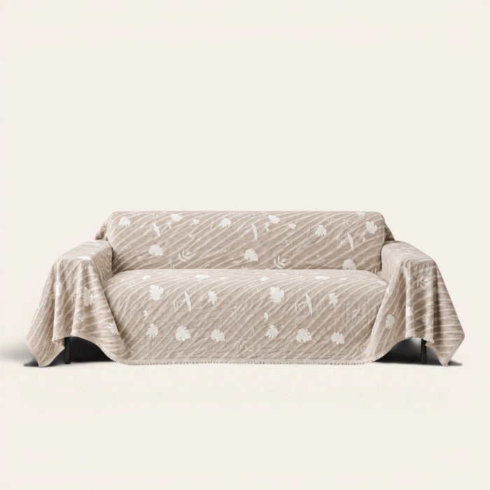 Linen Beige Botanical Quilted sofa throw draped over a two-seat sofa, front view on ivory background, white leaf motifs