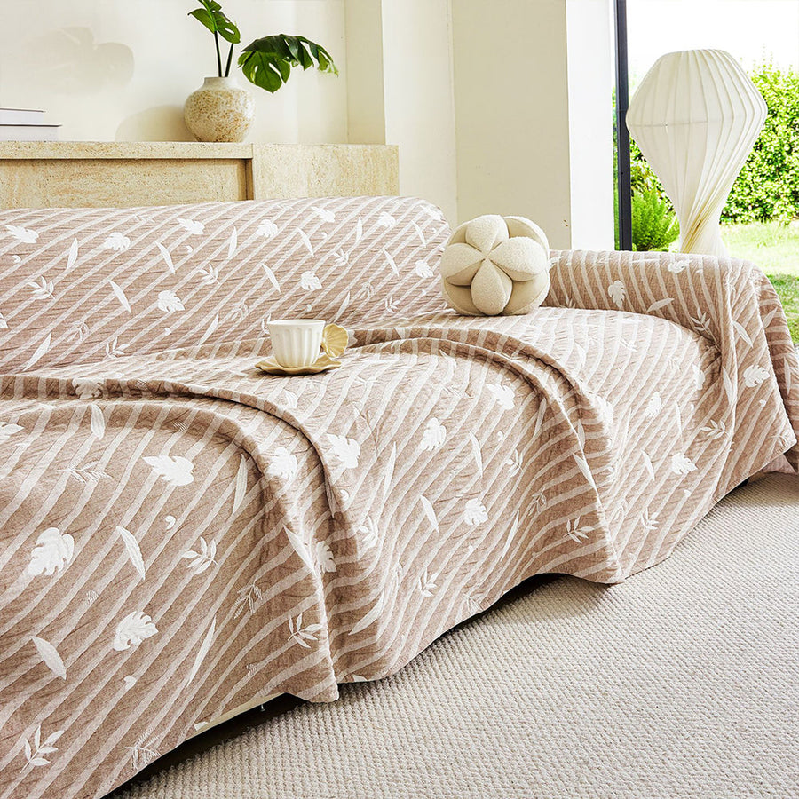 Linen Beige Botanical Quilted throw over a sofa with a flower cushion and teacup beside a sunlit window