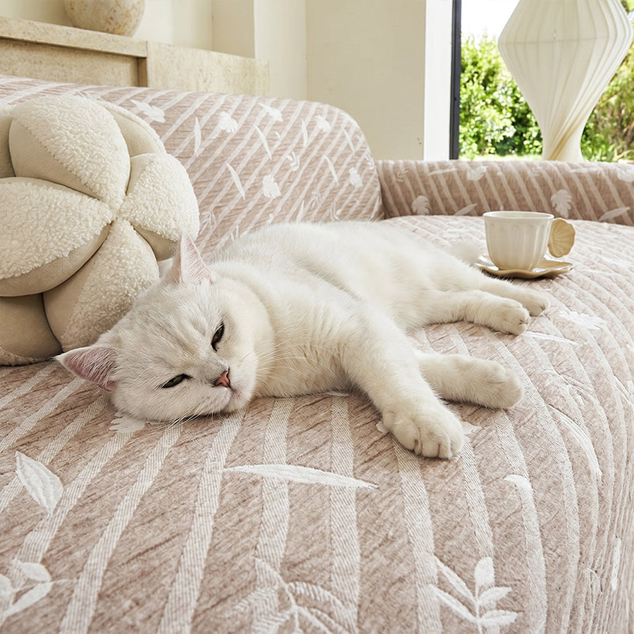 Close-up of Linen Beige Botanical Quilted throw with a white cat resting, showing the quilted leaf texture